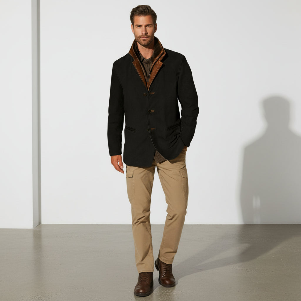 Man wearing a black coat with brown lining, beige pants, and brown shoes against a white background